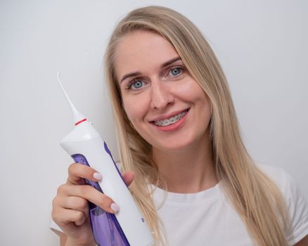 Portrait of a caucasian woman with braces on her teeth holding an irrigator