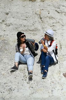 Joyful middle aged women sitting on the foothills and talking to etch other. Retirement active lifestyle, outdoor activity concept.