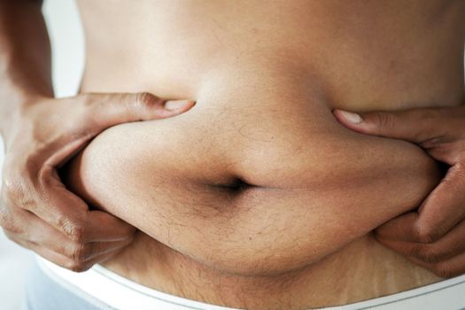 man's hand holding excessive belly fat, overweight concept.