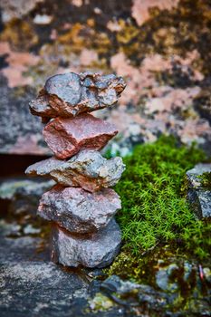Image of Focus on cairn stone stack of tiny rocks nested against mossy rocks and green tiny plants
