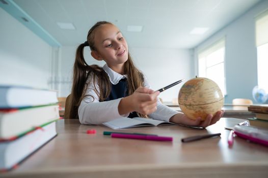 Caucasian schoolgirl sits at her desk at school and studies the globe