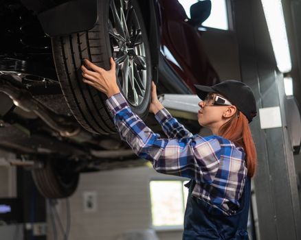 Female mechanic adjusting the tire of the car that is on the lift. A girl at a man's work