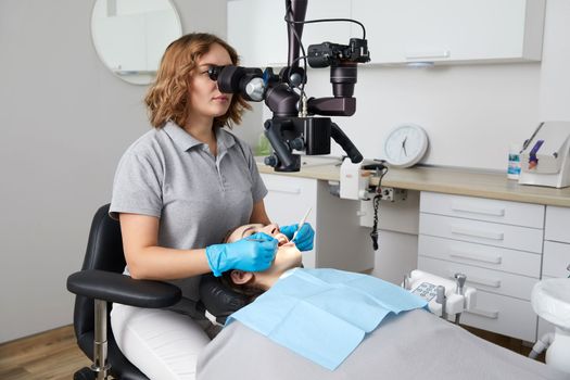 Female dentist with dental tools and microscope treating patient teeth at dental clinic office. Medicine, dentistry and health care concept. Dental equipment