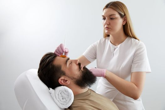 Cosmetologist applying a clay mask to male face. Spa treatment and face care in the beauty salon for men