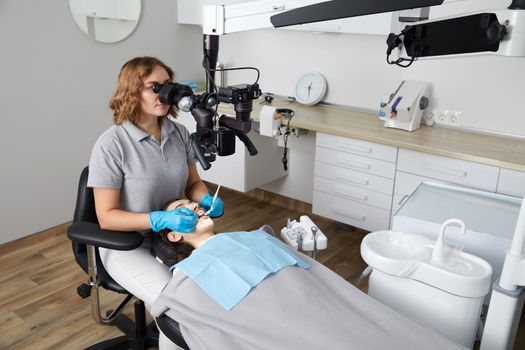 Female dentist with dental tools and microscope treating patient teeth at dental clinic office. Medicine, dentistry and health care concept. Dental equipment