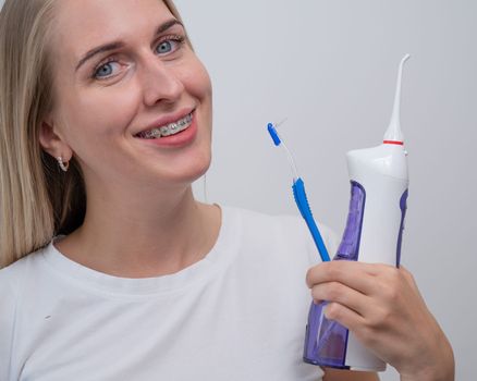 Smiling caucasian woman with braces on her teeth holding an irrigator and a toothbrush