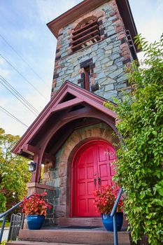 Image of Front entrance to stone church with huge double red doors and steeple with greenery