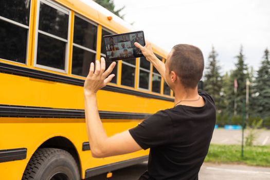 male Teacher Or Student With Digital Tablet near the school bus. video chat.