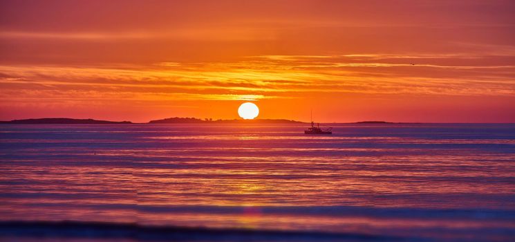 Image of Golden light over east coast ocean with sunrise and detail of sun and fishing ship in distance