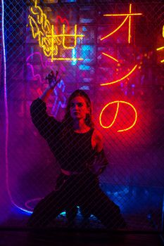 Caucasian woman in neon studio behind chain-link mesh