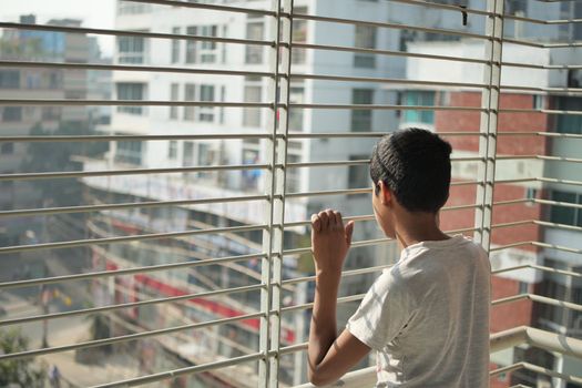 sad teenage boy looking through window .