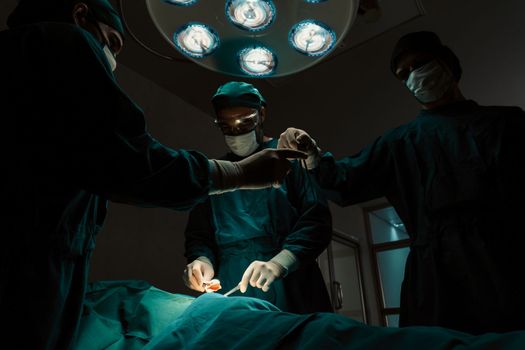 Surgical team performing surgery to patient in sterile operating room. In a surgery room lit by a lamp, a professional and confident surgical team provides medical care to an unconscious patient.