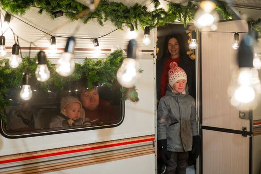 Caucasian family of 4 is celebrating Christmas in a van. Parents and two sons