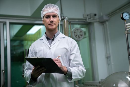 Apothecary scientist using a clipboard and pen to record information from a CBD oil extractor and a scientific machine used to create medicinal cannabis products.