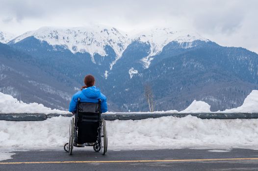 Rear view of a woman in a wheelchair travels in the mountains in winter