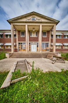 Image of Old abandoned building exterior with stone pillars and brick with overgrown fields