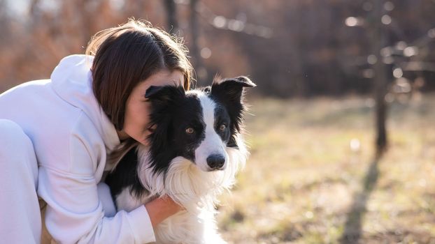 Caucasian woman hugging her dog Border Collie while sitting on a bench in autumn park