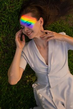 Top view of caucasian woman with rainbow ray on her face lies on green grass