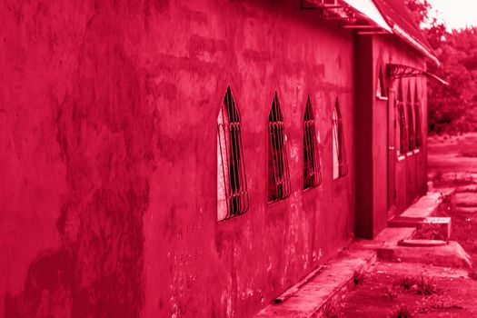 Beautiful red wall of the building. Red building with unusual Windows. Windows with interesting bars.Viva Magenta Background color