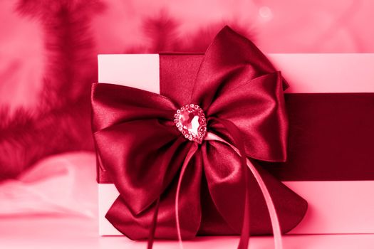 A Christmas gift decorated with a beautiful bow on a light background with a fir twig. Gifts, joy, surprise. Selective focus. the concept of Christmas and New Year. Viva Magenta Background color