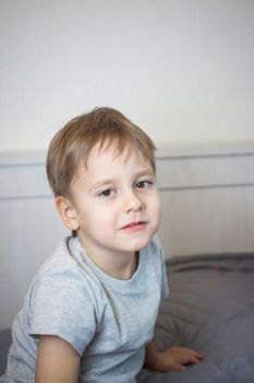 A photo of a handsome boy in a gray T-shirt looking at the camera. Portrait in a bright room. Natural, not staged photography. Children