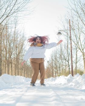 Smiling plump redhead woman jumping in park in winter