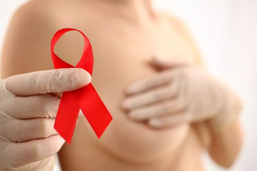 Woman with naked beautiful breasts holds red ribbon. Breast cancer concept