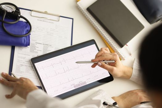 Doctor looks at ECG on tablet computer in cardiology center. Diagnosis of cardiovascular disease concept