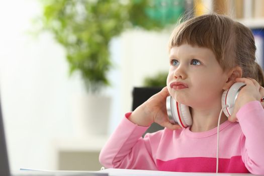 Beautiful cute little girl child in front of monitor in headphones. Watching cartoons or learning video concept