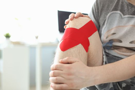 Male hands hold sore knee with kinesio tape sticker closeup. Injuries and sprains of knee joint and treatment
