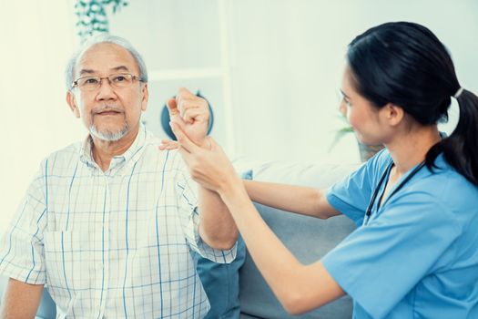 Caring young female doctor performing osteopathy treatment for a contented senior patient. At-home medical treatment for an Asian senior patient, joint pain treatment, medical service for seniors.