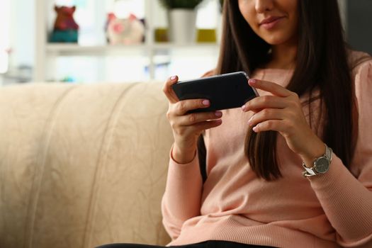 Woman sits on sofa and looks at smartphone. Browsing social networks and chatting correspondence concept