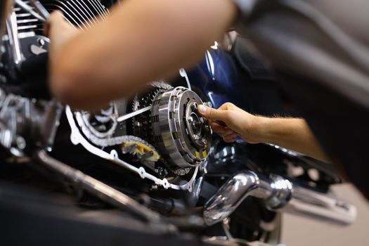 Mechanic repairs motor and chain of motorcycle in workshop. Motorcycle engine repair diagnostics concept