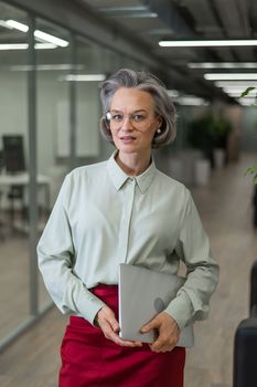 Mature caucasian woman stands with a laptop among the office
