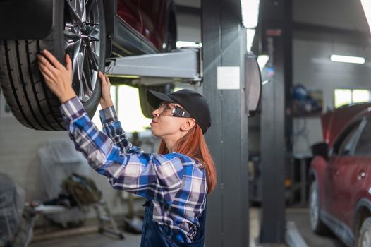 Female mechanic adjusting the tire of the car that is on the lift. A girl at a man's work