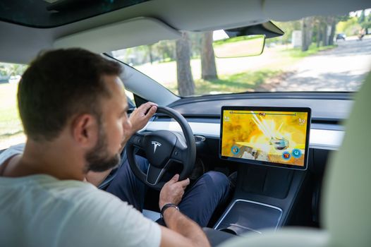 Novosibirsk, Russia - 10.08.2022: Caucasian man playing games while driving tesla car