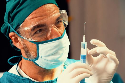 Surgeon fill syringe from medical vial for surgical procedure at sterile operation room. Doctor in full protective wear for surgery prepare anesthesia injection for his patient