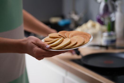 Woman holds plate with fresh delicious pancakes in kitchen. Making pancakes at home concept