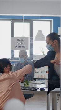 Coworkers touching elbow to avoid infection with coronavirus, business team wearing medical face mask while sitting on table desk working on company project respecting social distance