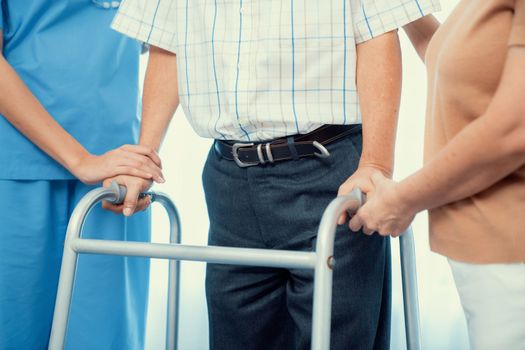 Contented senior man walking as he is helped by his wife and caretaker, walking with the aid of a folding walker. Nursing home for the elderly concept.