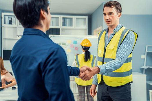 An engineer with a protective vest handshake with an investor in his office. Following a successful meeting, employee and employer form a partnership.