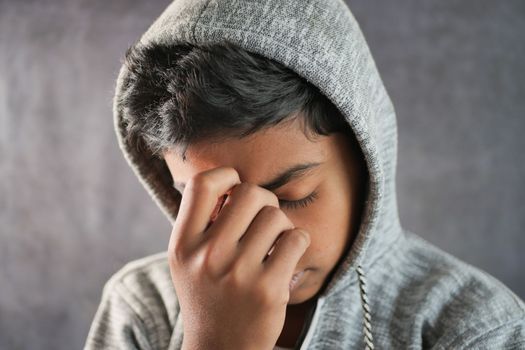 sad teenage boy covering his face sitting on sofa ,