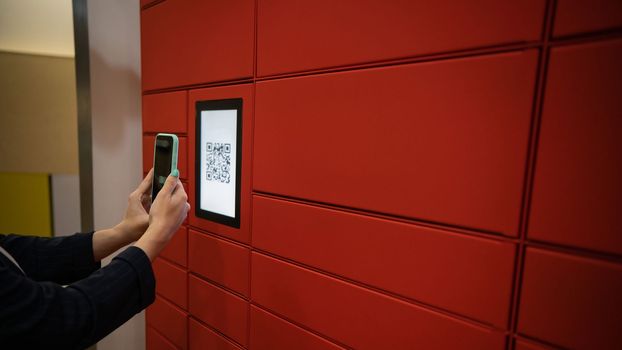 A woman scans a red code to pick up a parcel at a parcel machine. Automated Postal Box