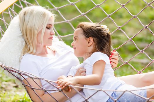 loving family spends time together in summer time enjoy the little things. slow life. mom and little daughter relax in a hammock in the summer in the garden.