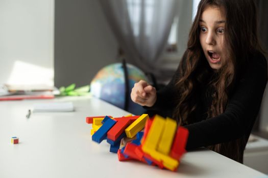 a little happy girl is playing the board game at the table. Construction of a tower made of wooden cubes.