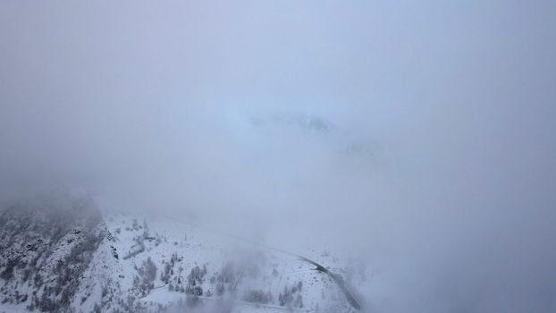 Snowy mountains with coniferous trees in the clouds. Medeo Dam. Everything is in fog and snow. Christmas and New Year have come. Aerial view from the drone on road, dam and trees. Almaty, Kazakhstan