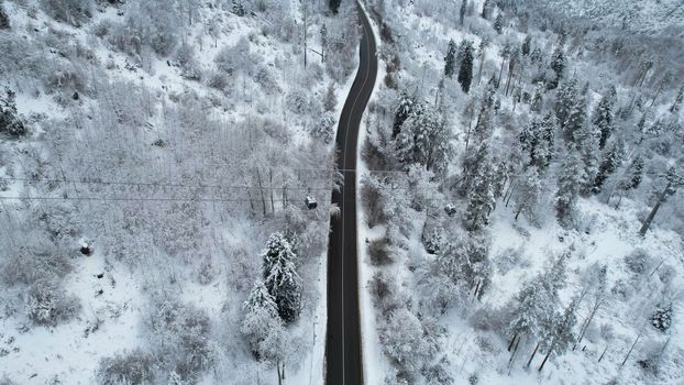 Cable car in the mountains in the winter forest. The cabins move along the gondola road through the winter snow forest and fog. White clouds covered the mountains. Top view from a drone. Medeo, Almaty