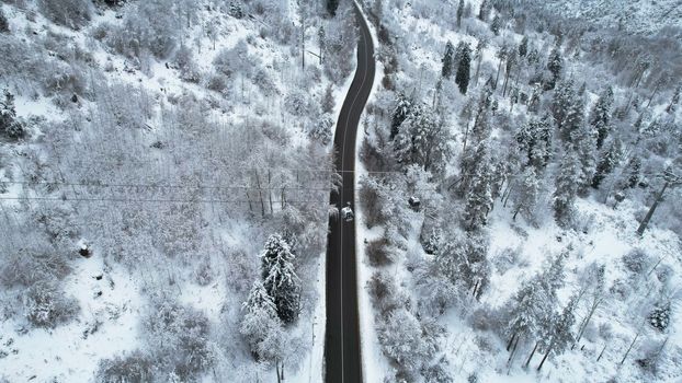 Cable car in the mountains in the winter forest. The cabins move along the gondola road through the winter snow forest and fog. White clouds covered the mountains. Top view from a drone. Medeo, Almaty