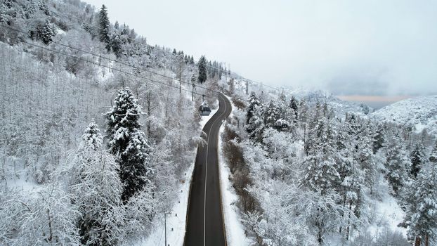 Cable car in the mountains in the winter forest. The cabins move along the gondola road through the winter snow forest and fog. White clouds covered the mountains. Top view from a drone. Medeo, Almaty