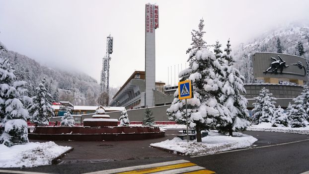 Winter alpine skating rink Medeo in the mountains. Drone view of the snowy forest and mountains. White clouds and fog in the gorge. Snow removal is underway. A large stadium. Almaty, Kazakhstan